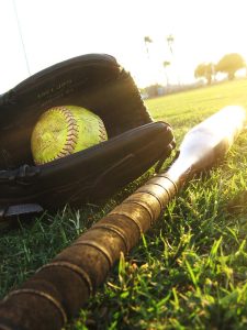 Softball glove, ball and bat laying on softball field grass