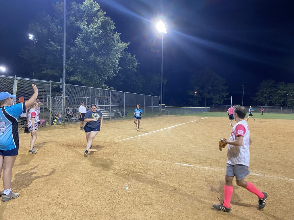 A group of people playing Coed Rec softball at night.