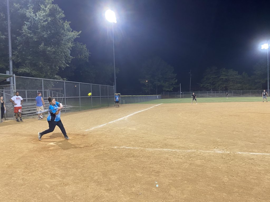 A group of people playing softball at night for NSA Softball Team Photos.