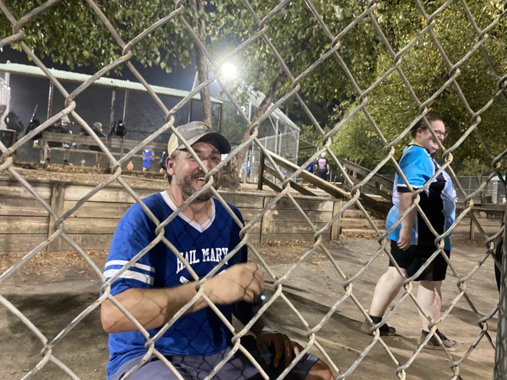Brendon sitting behind a chain link fence sipping what is definitely a soda