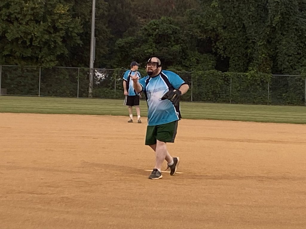 Brent in a blue shirt pitching a softball on a field in Richmond, Virginia.