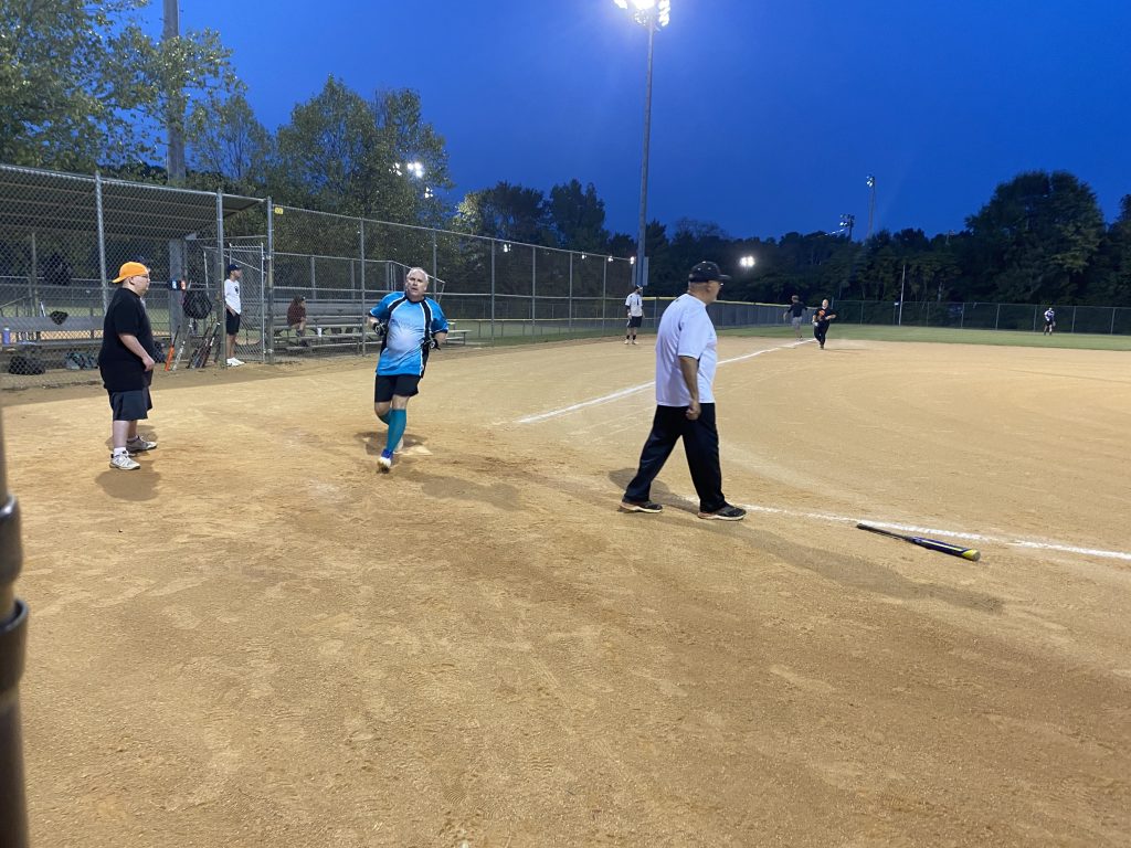 A group of people on a softball field at night playing NSA Softball.