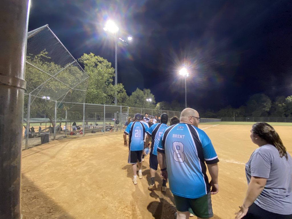 A group of people walking on a baseball field at night taking Richmond Virginia softball photos.