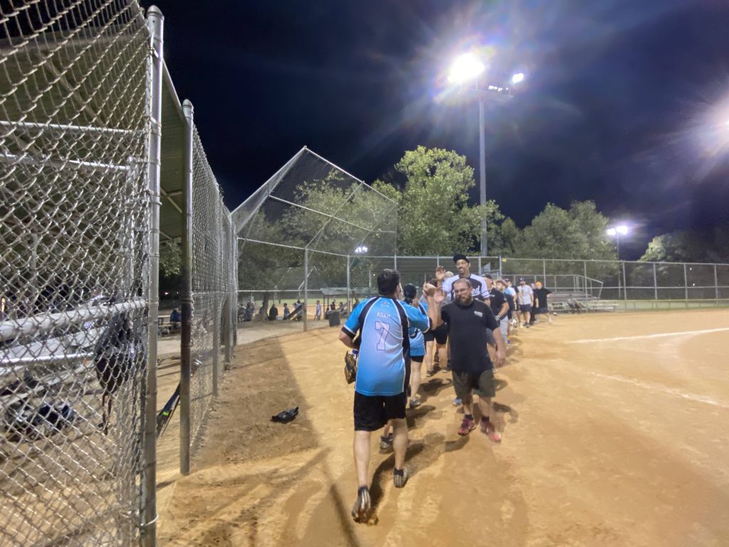 A group of people from the NSA Softball Team, Hail Mary, walking on a softball field at night.